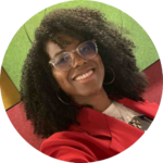 Picture of Miljorha Martin. A beautiful black woman with long curly hair, wearing glasses and a red jacket.