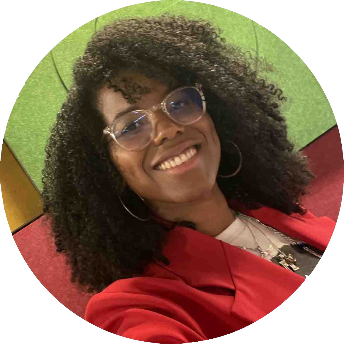 Picture of Miljorha Martin. A beautiful black woman with long curly hair, wearing glasses and a red jacket.