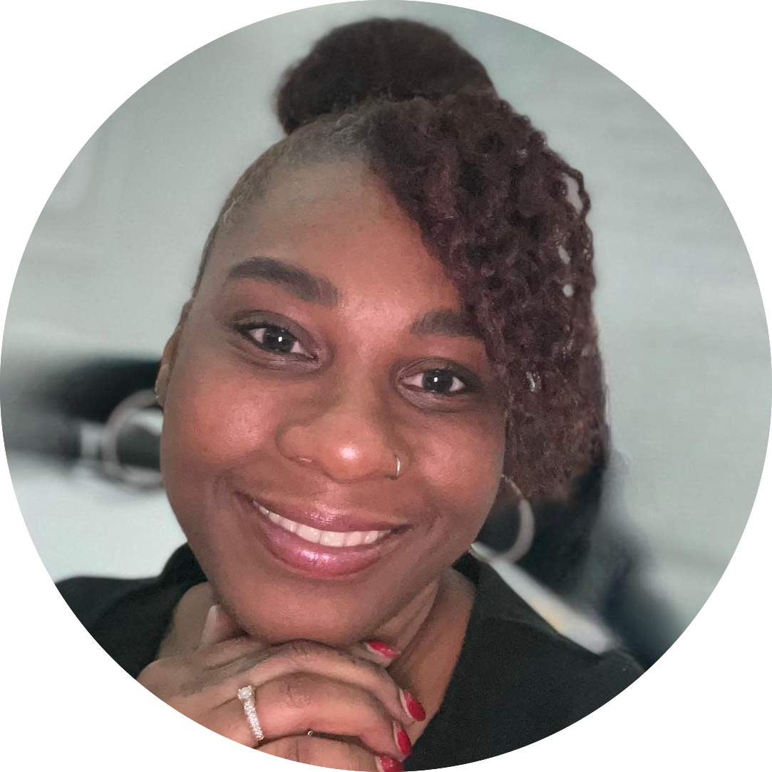 Picture of Saskia Sambo. A beautiful black woman with brown curly hair in a updo, wearing a black jacket
