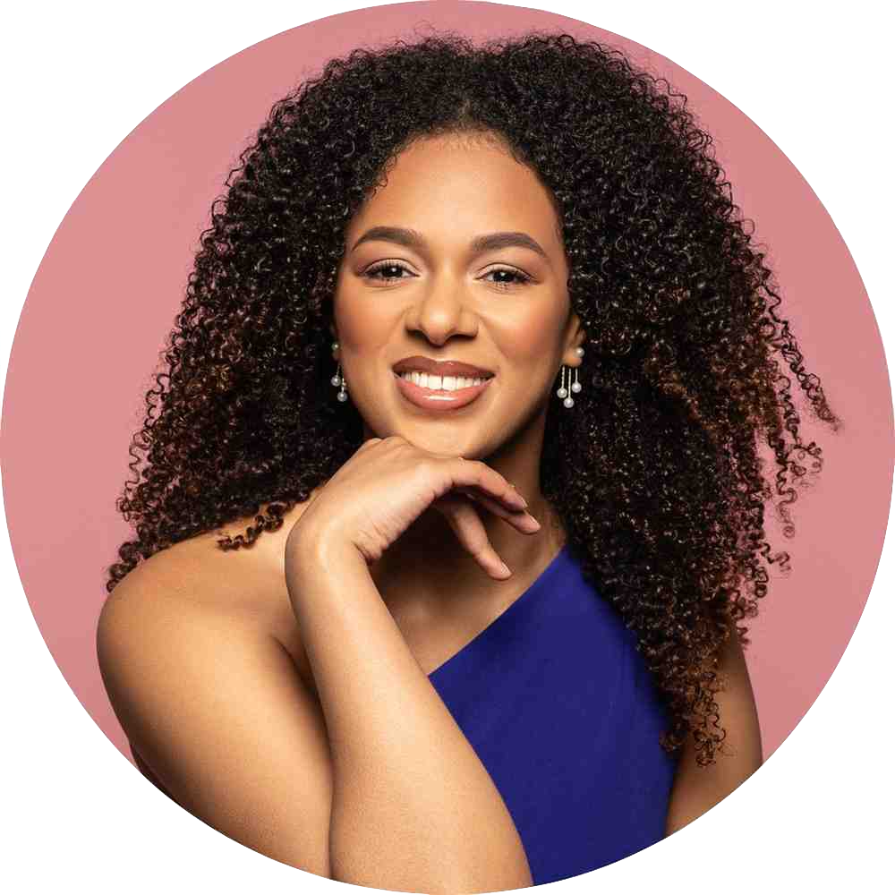 Picture of Sharesca Clara. A beautiful black woman with long curly hair and a blue top. Picture has a pink background.