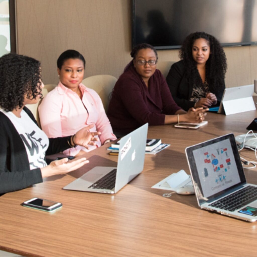 zvvt relief promo image - 4 black women in a business meeting with laptops on a wooden desk.