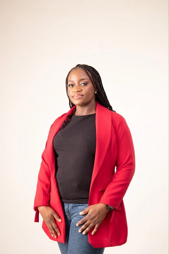 Picture of Omolola Fagade. A beautiful black woman with black braids, wearing a black top and red jacket.