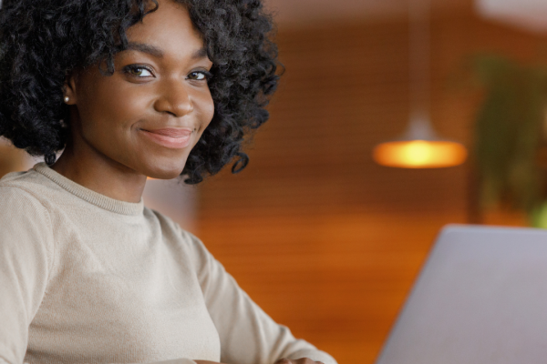 Homepage Black woman with afro hair and a white sweater, behind a laptop